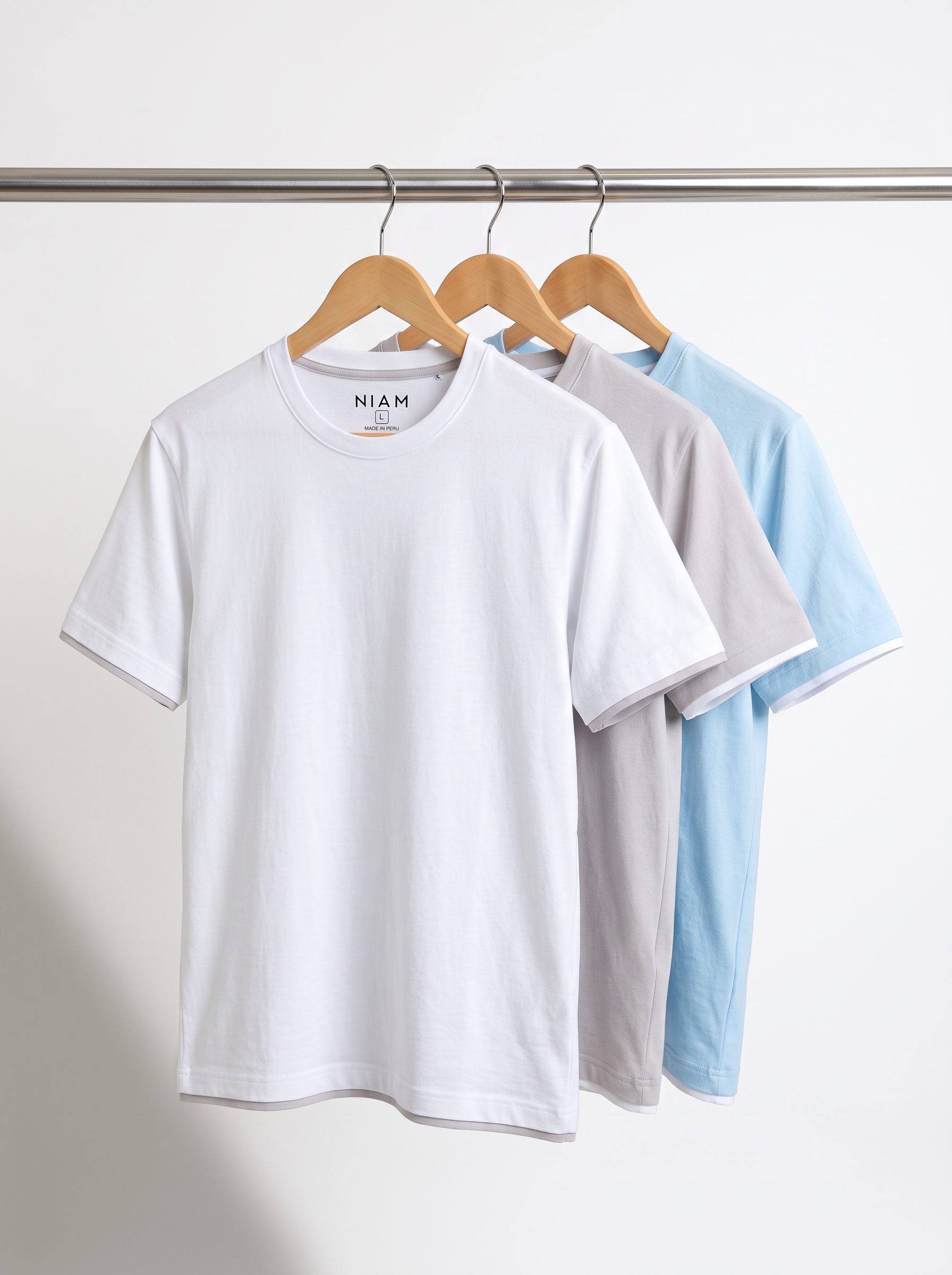Three contrast crewneck tees in white, light gray and light blue on a studio rail